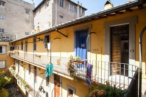 A yellow building with a balcony, a wooden door, and a window with a curtain.