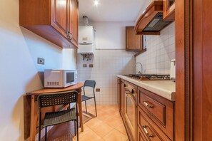 A compact kitchen with wooden cabinets, a microwave, a gas stove, and a small dining area with a chair.