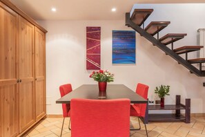 A dining area with a wooden cabinet, a table with red chairs, and a staircase with wooden steps.
