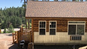 Una cabaña rústica con terraza de madera, varios ventanales y techo de metal.