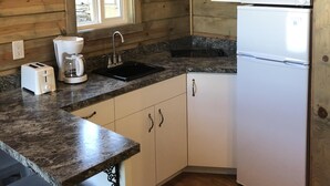 Una cocina pequeña con paredes de madera, una ventana, un lavamanos, un microondas, una cafetera y un refrigerador.