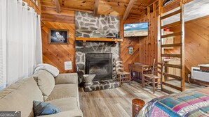 Ein gemütliches Cabin-Interieur mit Kamin aus Stein, Holzwänden, einer Couch und einem Bett.