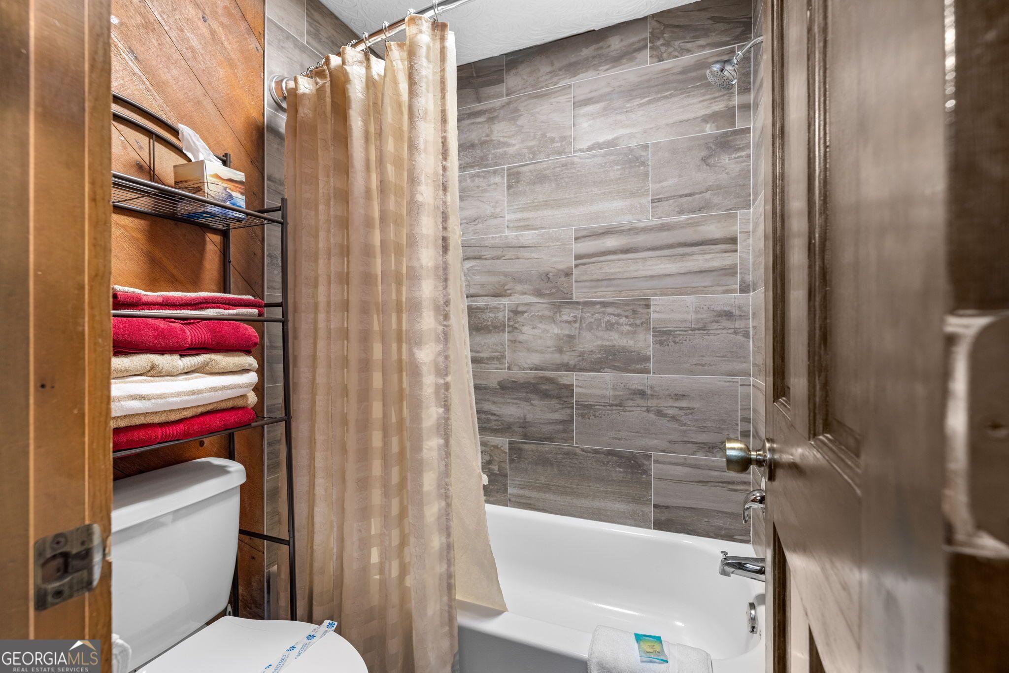 A bathroom with a shower, a toilet, and a towel rack with folded towels.