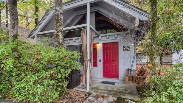 Eine kleine Holzhütte mit roter Tür, umgeben von Bäumen und einer Holzbank.