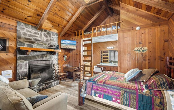 Un chalet confortable avec une cheminée en pierre, un lit superposé, un bureau et un téléviseur.