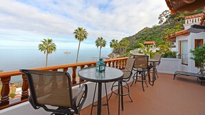 A balcony with outdoor seating, overlooking a body of water and a hillside. - H890: Breathtaking ocean front villa, 2 Fireplaces, Cart, King Bed, VIEWS (Avalon)