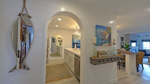 A modern kitchen with white cabinetry, a central island, and a dining area with wicker chairs. - H890: Breathtaking ocean front villa, 2 Fireplaces, Cart, King Bed, VIEWS (Avalon)