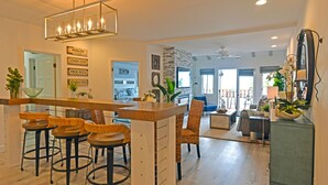 A modern kitchen with a bar area, bar stools, and a dining area with a sofa and chairs. - H890: Breathtaking ocean front villa, 2 Fireplaces, Cart, King Bed, VIEWS (Avalon)