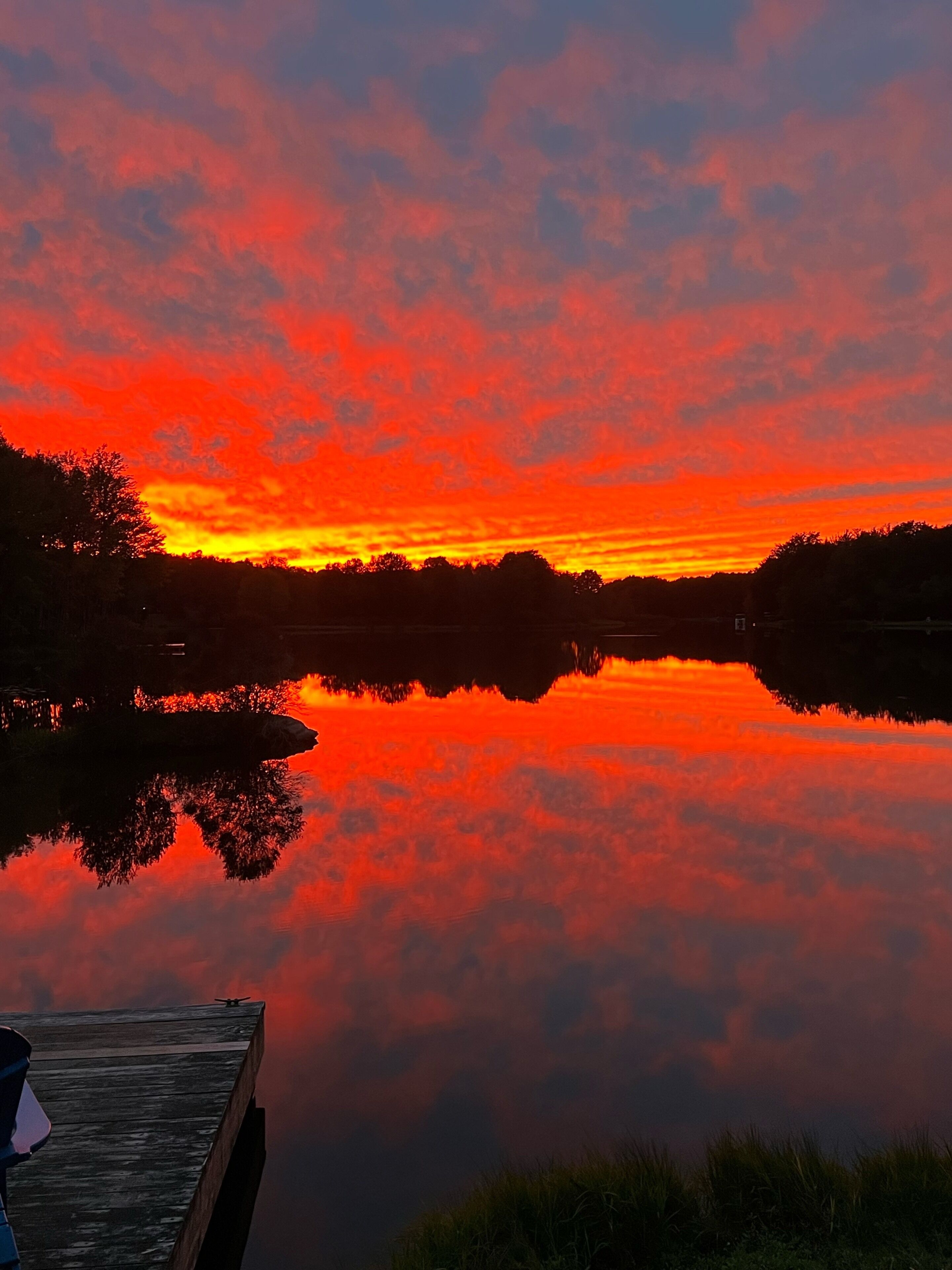 Un tramonto sul lago calmo, con un pontile e alberi sullo sfondo.