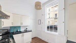 A modern kitchen with white cabinetry, a black countertop, a stainless steel stove, and a window with a view of the street. - Garden maisonette in Bath city centre (Bath)