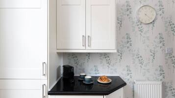 A kitchen with white cabinets, a black countertop, a coffee maker, two cups, and a plate with food.