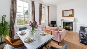 A dining area with a table set for four, a pink sofa, and a television in the background. - Garden maisonette in Bath city centre (Bath)