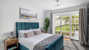 A bedroom with a large bed, a nightstand, a potted plant, and a view of a garden through a sliding glass door. - Garden maisonette in Bath city centre (Bath)