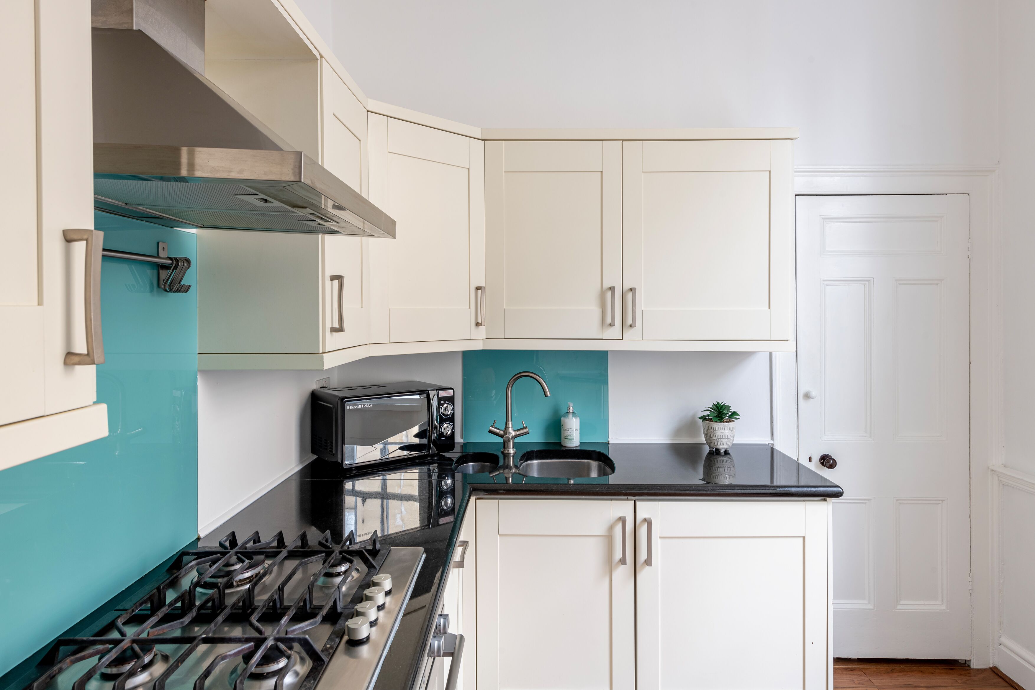 A compact kitchen with white cabinets, a black countertop, a stove, a toaster, and a sink.