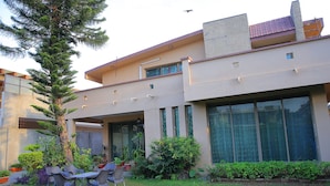 A modern building with a large glass window, a patio with chairs, and a well-maintained garden. - Shawnze House (Islamabad)
