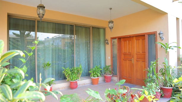 A balcony with potted plants, a wooden door, and a large window with curtains. - Shawnze House (Islamabad)