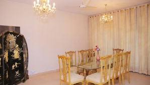 A dining room with a glass table surrounded by ornate chairs, a black decorative cabinet, and two chandeliers. - Shawnze House (Islamabad)