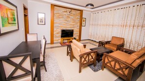 Una sala de estar con televisor, muebles de madera y un papel tapiz estampado.
