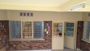 A room with brick walls, a tiled floor, a window with bars, a door with a window, and a small table. - Feel At Home (Kigali)