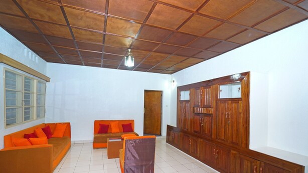 A spacious room with a high ceiling, tiled floor, and a large wooden wardrobe. - Feel At Home (Kigali)