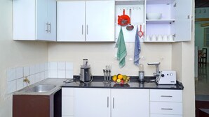 A kitchen with white cabinets, a black countertop, a fruit bowl, a coffee maker, and a toaster. - Feel At Home (Kigali)
