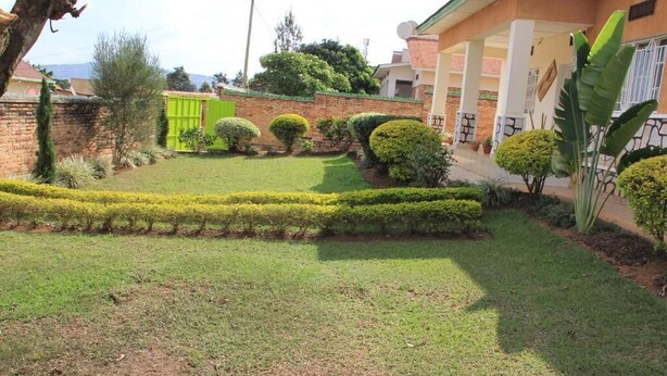 A well-maintained garden with neatly trimmed hedges, a brick wall, and a building with a tiled roof. - Joy Guesthouse (Kigali)