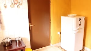 A kitchen with a brown door, a white refrigerator, and a wooden table with pots. - Joy Guesthouse (Kigali)
