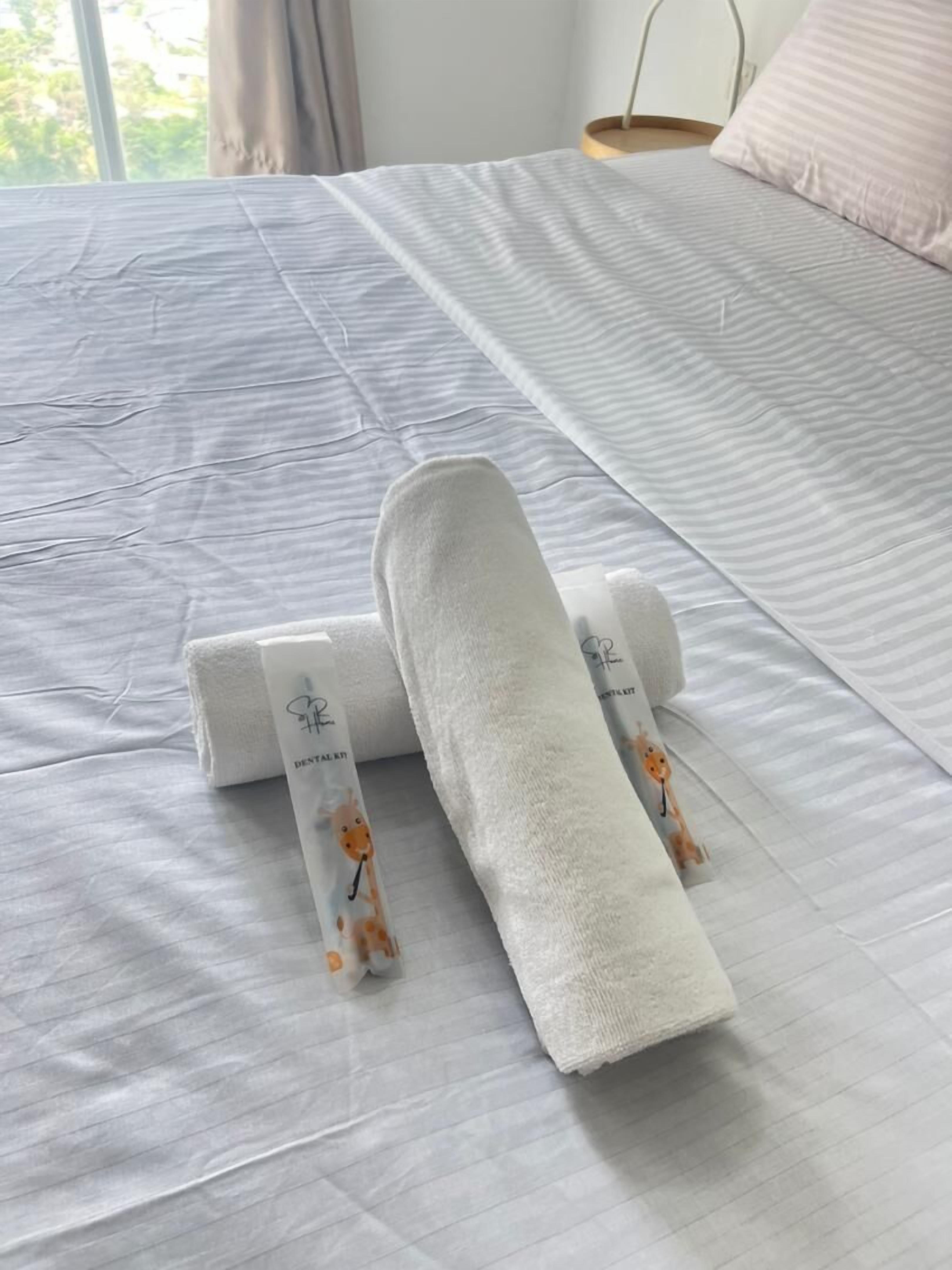 A neatly made bed with a white bedspread and two rolled towels with giraffe prints.