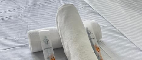 Una cama bien hecha con una colcha blanca y dos toallas enrolladas con estampado de jirafa.