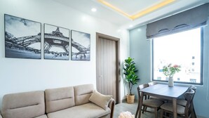 A living room with a sofa, a dining table with chairs, a potted plant, and two framed pictures of the Eiffel Tower. - 7S Hotel Hoang Anh & Apartment (Nam Nha Trang)