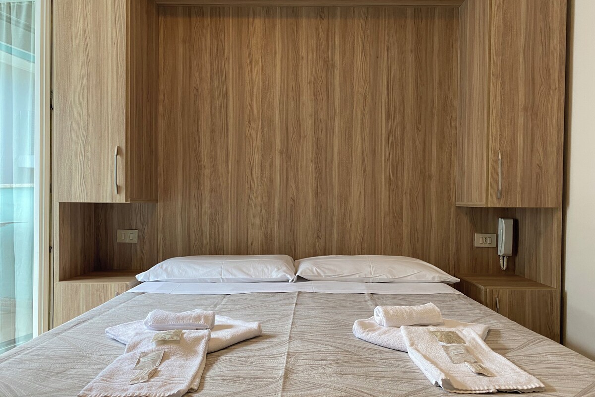 Ein Hotelzimmer mit einem hölzernen Kopfteil, zwei Nachttischen, einem Bett mit weißer Bettwäsche und einem Telefon auf dem rechten Tisch.