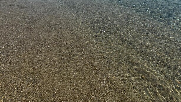 Una playa despejada con aguas poco profundas, una orilla arenosa y un paisaje montañoso lejano.