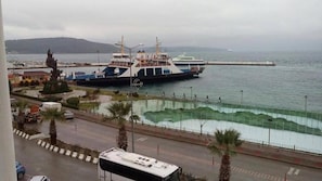 A ferry docked at a port with a view of the sea and a road with palm trees.