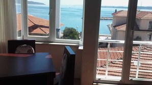 Habitación con un amplio ventanal que ofrece vista al mar y a edificios. Hay una mesa de madera y una silla en la habitación.