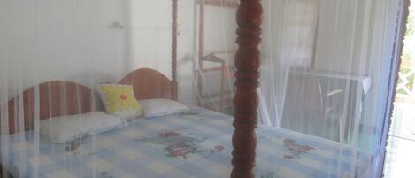 Una cama con una colcha estampada con motivos florales, un cabecero de madera y una mosquitera.