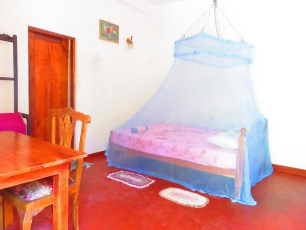 A room with a bed under a blue canopy, a wooden table, and a red floor. - Beach Lagoon Guest House (Tangalle)
