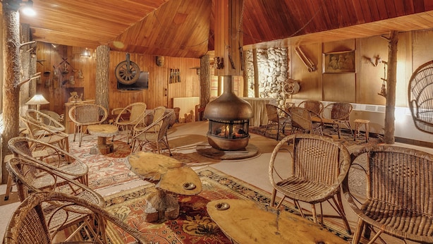 A rustic interior with wooden walls, a stone fireplace, wicker furniture, and a large wood stove. - Pahalgam hotel (Anantnag)