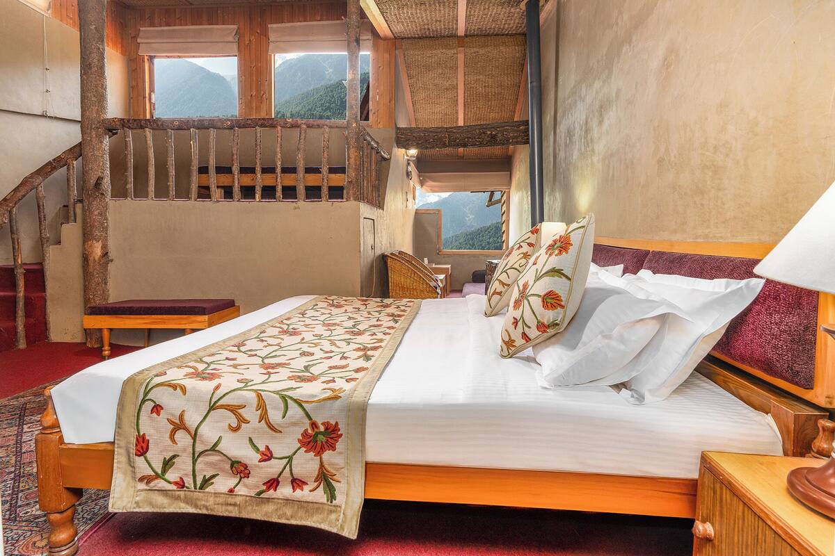 A bedroom with a wooden bed, a red carpet, a wooden chair, a nightstand, and a staircase with a wooden railing.