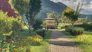 A garden pathway leading to a gazebo, surrounded by lush greenery and a mountain backdrop. - Pahalgam hotel (Anantnag)