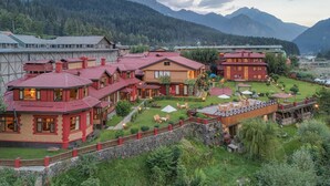 A traditional building with a red roof, surrounded by lush greenery and mountains in the background. - Pahalgam hotel (Anantnag)