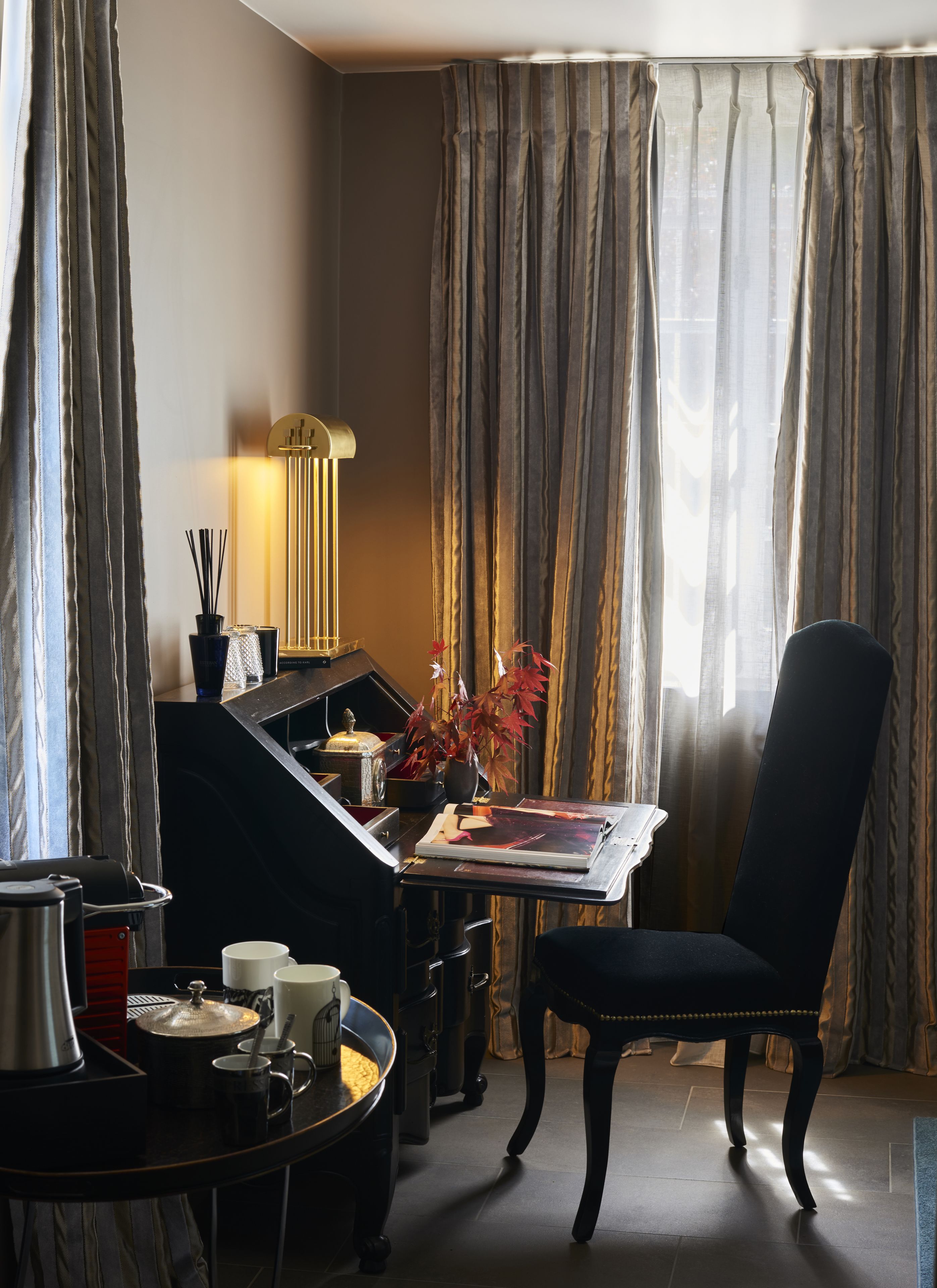 Habitación de hotel con una mesa de comedor, una silla, una lámpara y vistas a través de cortinas.
