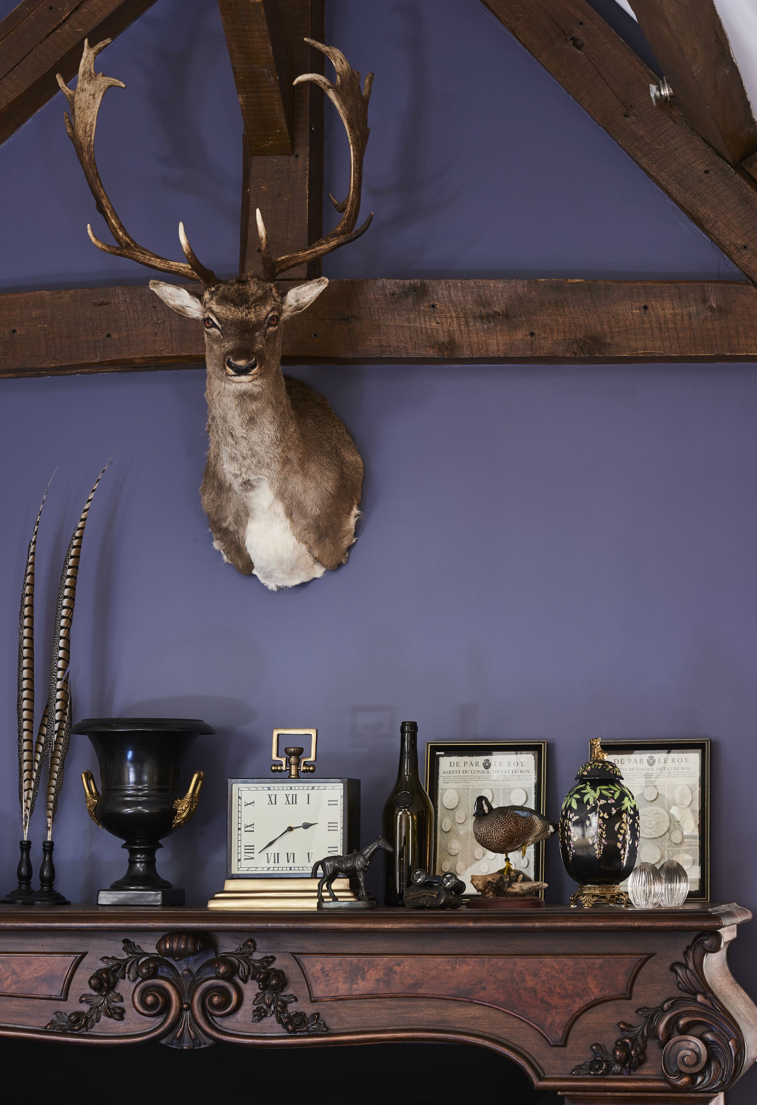 Una habitación con un ciervo montado en la pared, un reloj, objetos decorativos y estructura de vigas de madera.