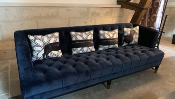 Un sofá azul oscuro con capitoné y cojines estampados, ubicado en una habitación con paredes de ladrillo visto y vigas de madera.