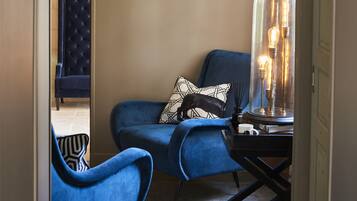 A room with a blue armchair, a black and white patterned pillow, and a table with a glass lamp.