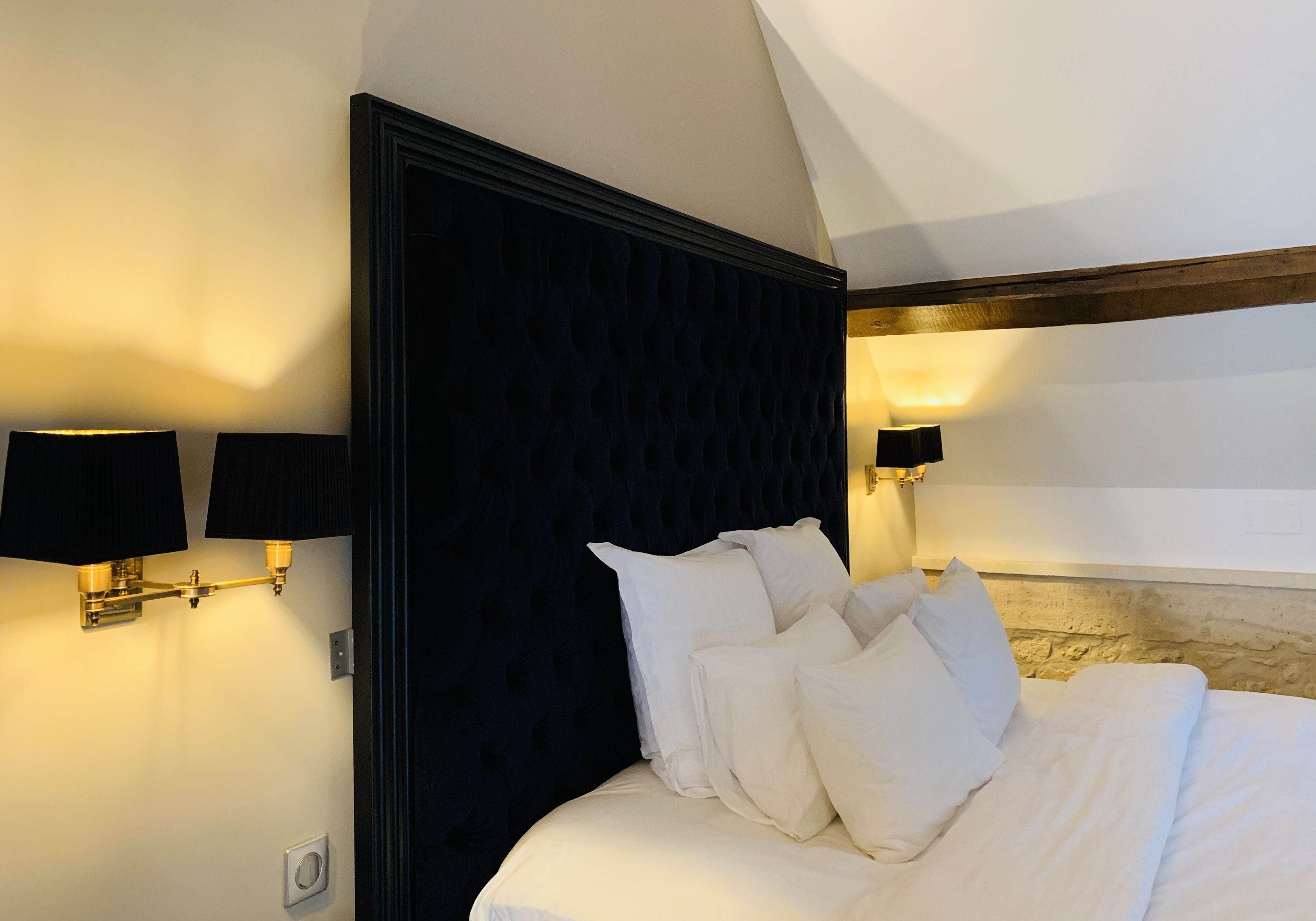 A bedroom with a dark headboard, white bedding, and wall-mounted lamps.