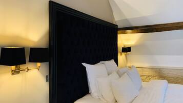 A bedroom with a dark headboard, white bedding, and wall-mounted lamps.
