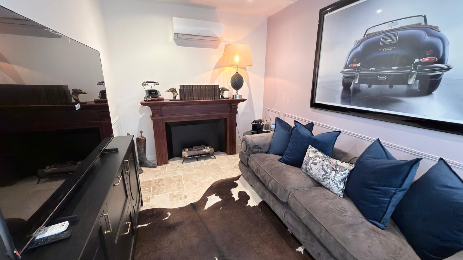A living room with a fireplace, a sofa with blue cushions, a television, and a framed picture on the wall.