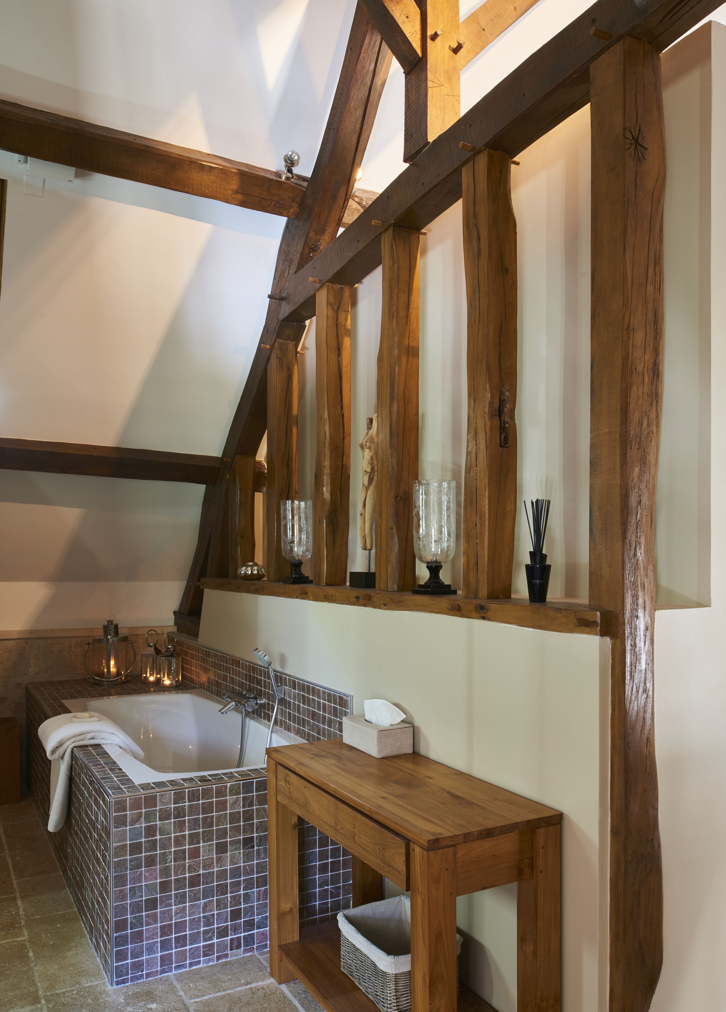 A bathroom with a large bathtub, wooden beams, and a tiled floor.