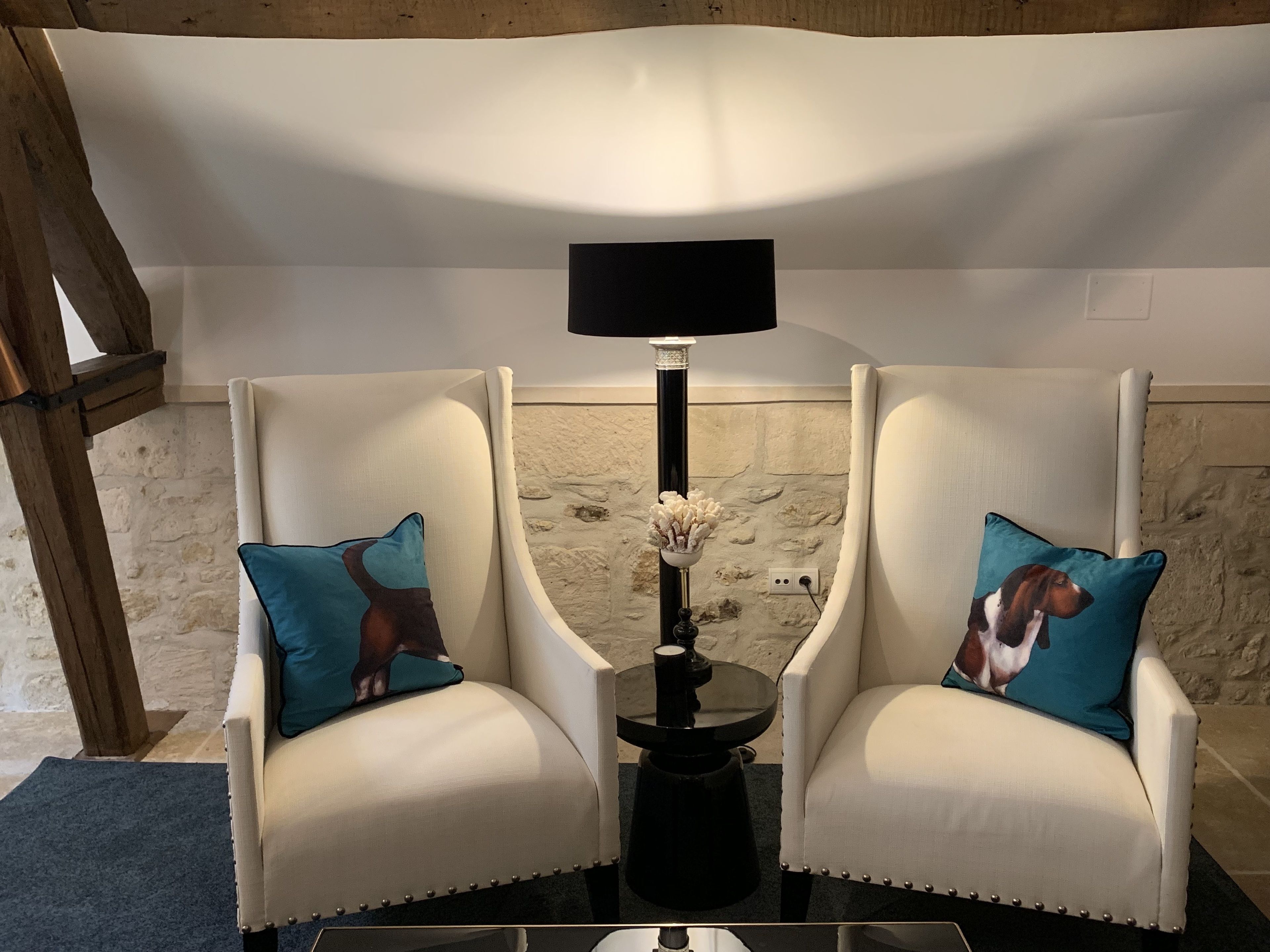 Two white armchairs with teal cushions, a black floor lamp, and a small table between them.