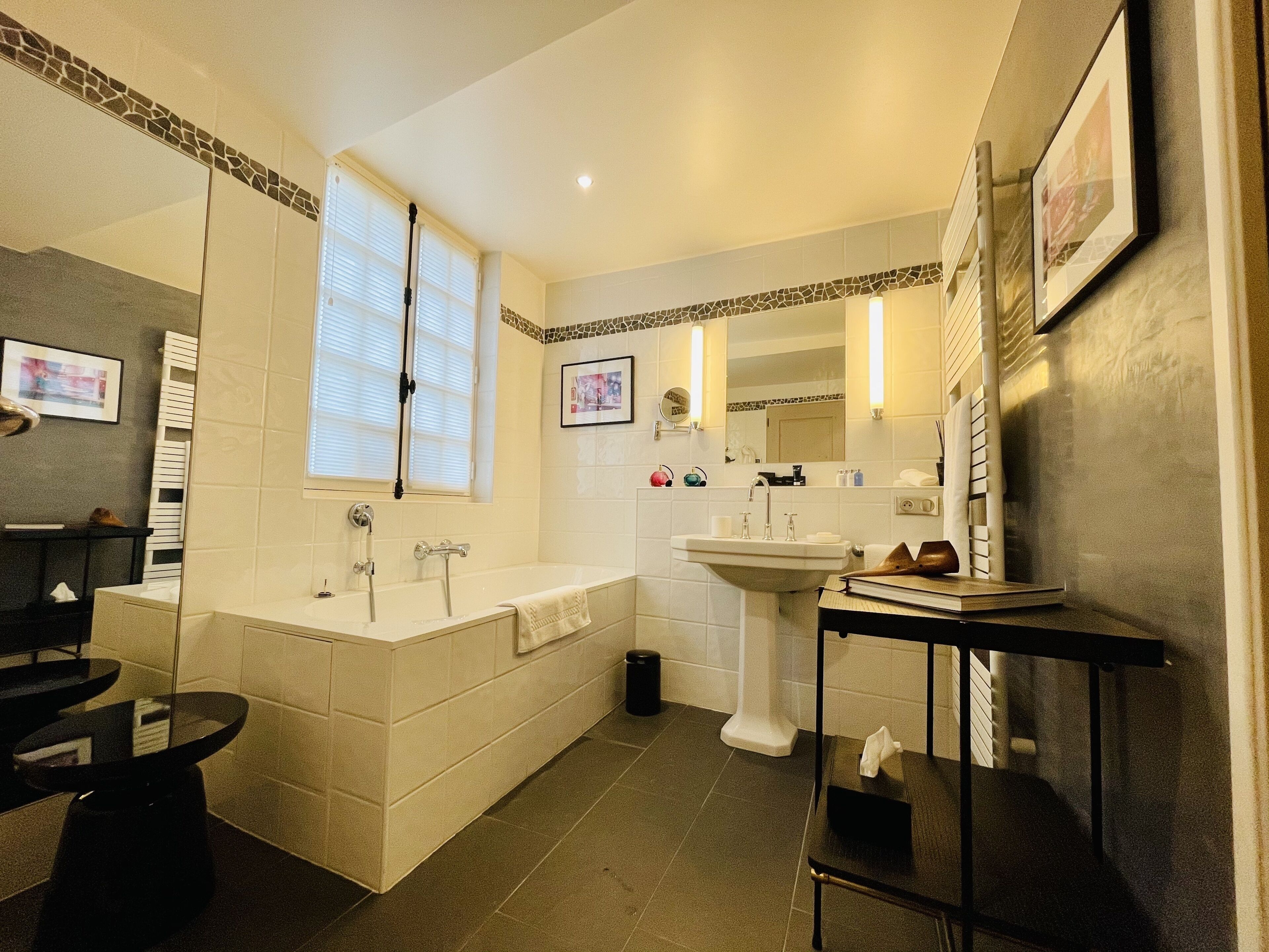 A modern bathroom with a bathtub, a sink, and a vanity. There are two windows with blinds, a mirror, and a towel rack.